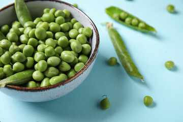 Bowl with fresh green peas on blue background