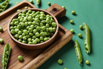Bowl and wooden board with fresh green peas on color background