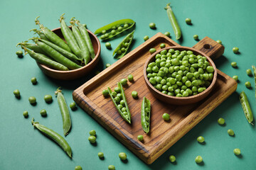 Bowls and wooden board with fresh green peas on color background