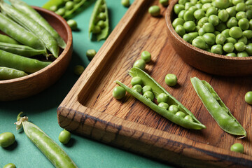 Bowls and wooden board with fresh green peas on color background, closeup