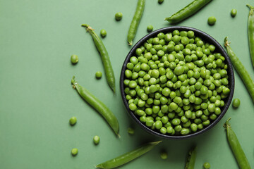 Bowl with fresh green peas on color background
