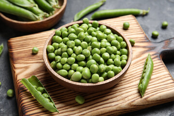 Bowls and wooden board with fresh green peas on black background