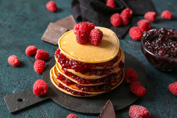 Board of tasty pancakes with raspberries on black background