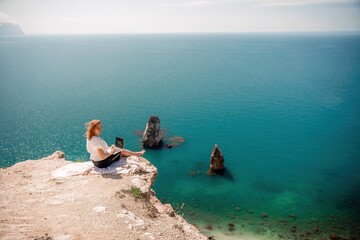 Freelance woman working on a laptop by the sea, typing away on the keyboard while enjoying the beautiful view, highlighting the idea of remote work.