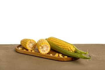Wooden board with fresh corn cobs and seeds on brown table against white background