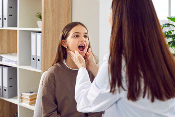 Child patient visits doctor. Woman pediatrician or otolaryngologist asks kid to open mouth and...