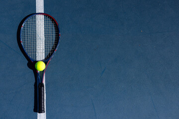 Overhead of tennis ball and tennis racket lying on tennis court on sunny day, copy space