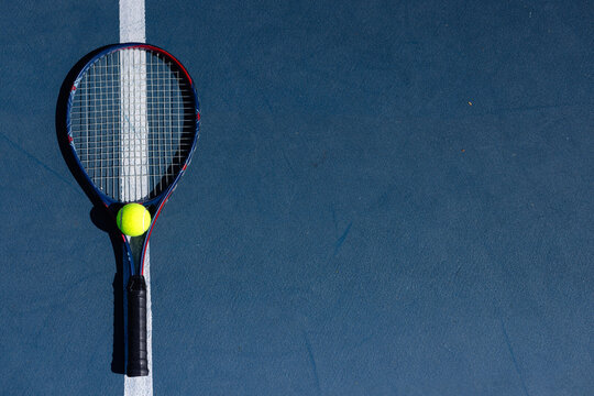 Overhead of tennis ball and tennis racket lying on tennis court on sunny day, copy space