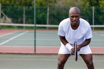 Portrait of focused african american male tennis player on outdoor court on sunny day, copy space