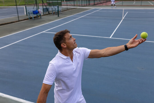 Caucasian male tennis player playing tennis serving ball on outdoor court