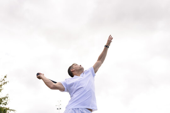 Caucasian male tennis player playing tennis serving ball on outdoor court on cloudy day