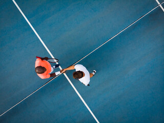 Overhead view of diverse male tennis players shaking hands on outdoor court, copy space