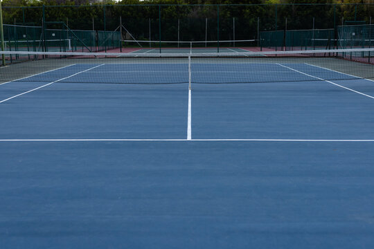 Empty blue surfaced outdoor tennis court with net and white markings, copy space