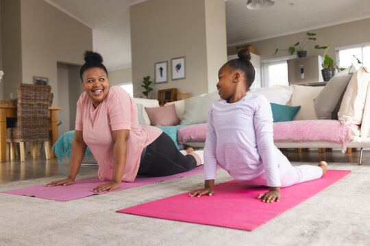 Happy african american mother and daughter doing yoga and stretching in living room