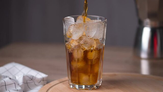 Pouring brewed coffee in a glass with ice cubes. Making iced latte or iced tea. Refreshing summer iced coffee or iced tea drink.