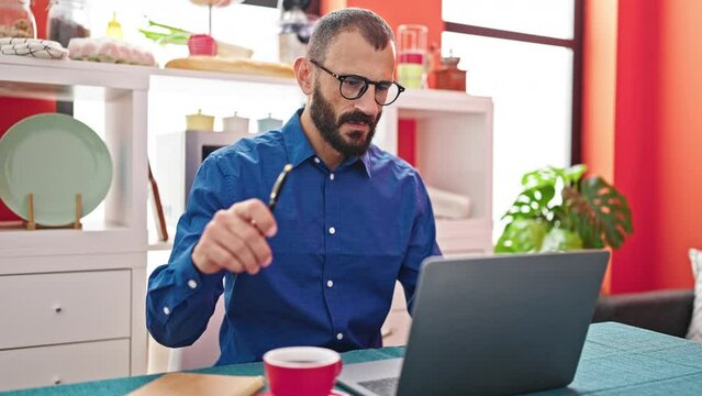Young hispanic man using laptop thinking at dinning room
