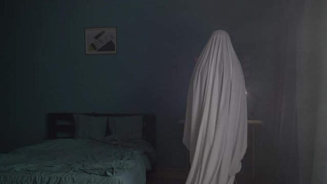 Ghost in apartment, man covered with a white sheet stands looking at a photo, Concept of a scary Halloween