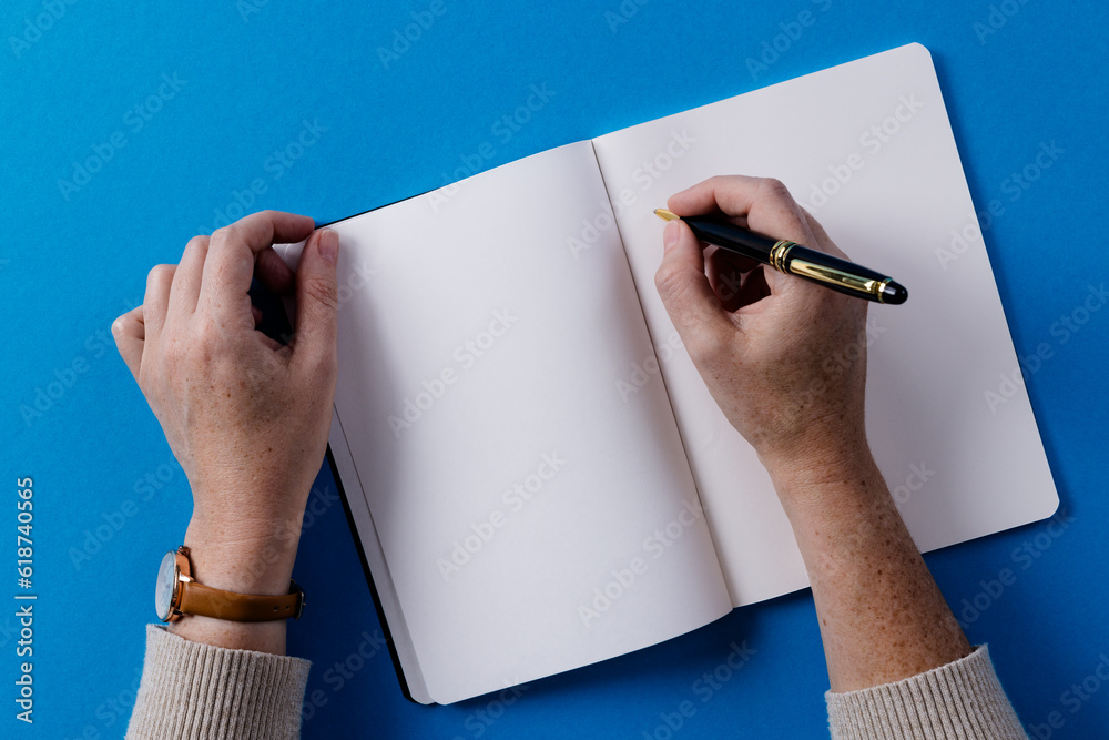 Poster Hands of caucasian woman holding pen and writing in notebook with copy space on blue background