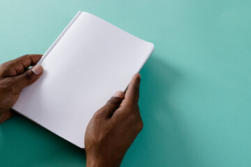 Hands of biracial man holding book with copy space on green background