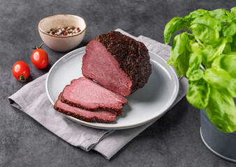 Seasoned smoked beef with  slices on a plate on dark background with fresh vegetables and herb. Natural meat snack
