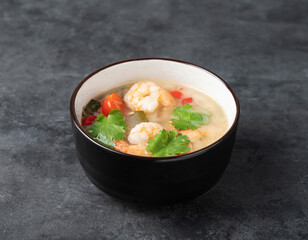 Tom yam soup with shrimp and chili pepper in a black bowl on a dark isolated  background. Traditional Asian food. Thai dish concept.