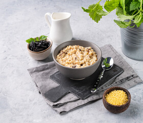 Millet porridge with prunes in a bowl on a light background with milk. The concept of a delicious and healthy breakfast. Dietary and energy food