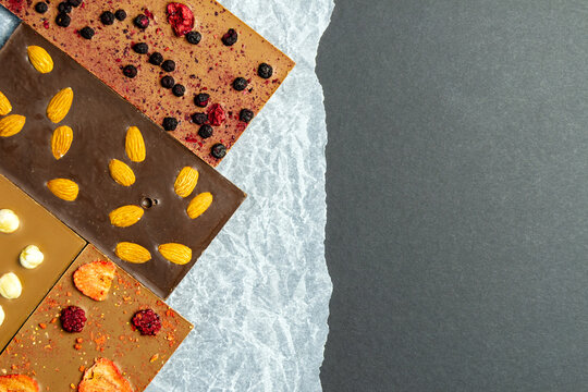 Chocolate bar with almonds, strawberries, raspberries and hazelnuts on a paper background. Sweetness with nuts. black space for inserting text. Horizontal image.