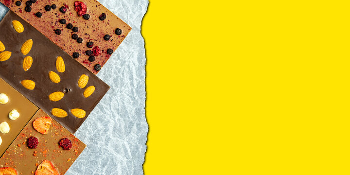 Chocolate bar with almonds, strawberries, raspberries and hazelnuts on a paper background. Sweetness with nuts. yellow space for inserting text. Horizontal image. Banner for insertion into site.