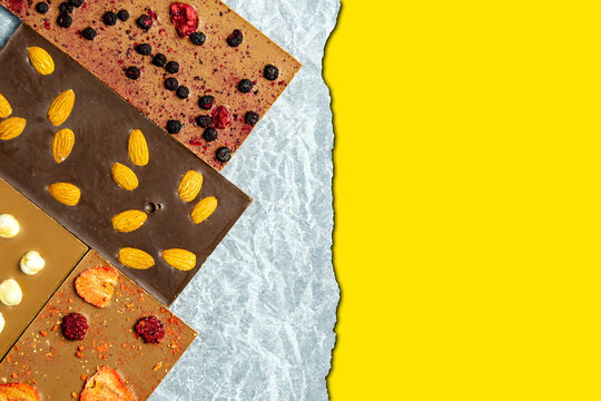 Chocolate bar with almonds, strawberries, raspberries and hazelnuts on a paper background. Sweetness with nuts. yellow space for inserting text. Horizontal image.