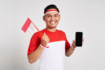 Smiling young Asian man in casual white t-shirt holding smartphone with blank screen and Indonesia...