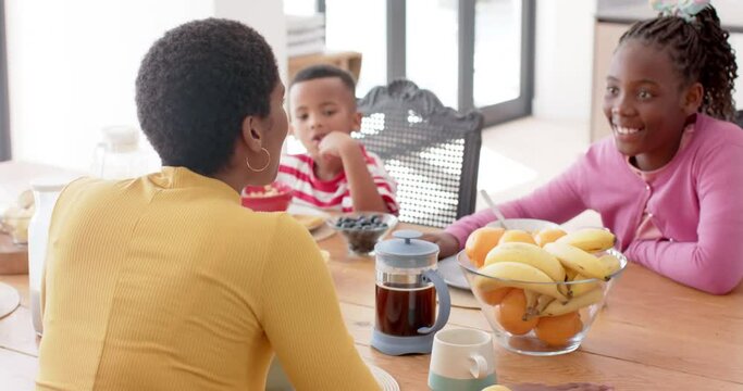 African american mother with son and daughter eating breakfast at table in kitchen, slow motion