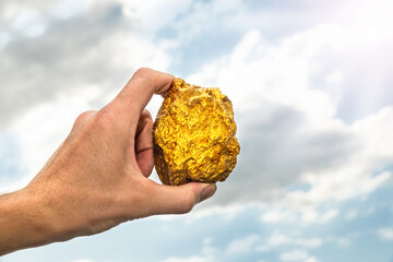 Gold nugget in a man's hand raised to the sky. The concept of wealth and success in the financial...