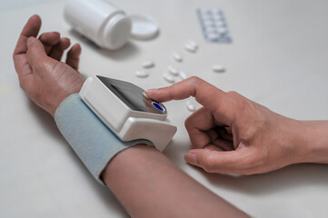 woman checks blood pressure. blood pressure monitoring at hand. Digital tonometry on a human hand. Pills, medicines on the table.