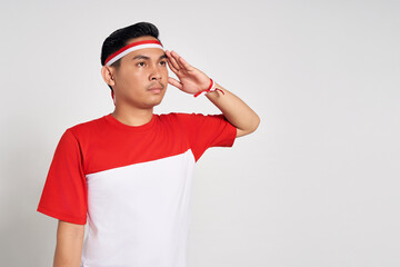 Young Asian man standing confidently giving salute and respectful gestures isolated over white background. Celebrate Indonesia independence day on 17 August