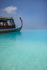 Fototapeta na wymiar Wooden sailing boat in crystal clear tropical lagoon bay close to beach of deserted exotic island. Maldives Dhoni boat, vertical panorama as luxury travel landscape, amazing vacation wallpaper concept