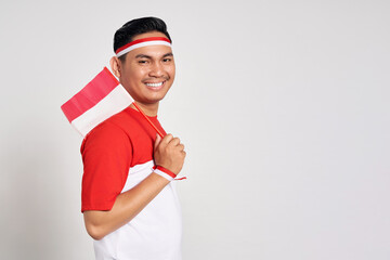 Smiling happy young Asian man holding an Indonesian flag isolated over white background. Celebrate...