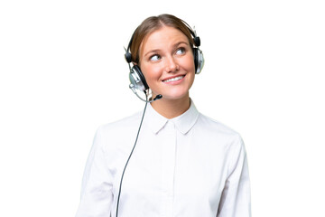 Telemarketer caucasian woman working with a headset over isolated background looking up while smiling