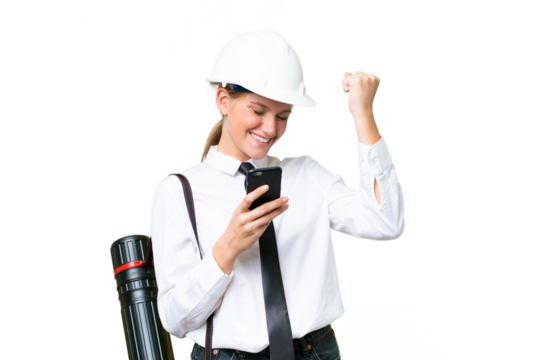Young architect caucasian woman with helmet and holding blueprints over isolated background with phone in victory position