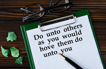 Do unto others as you would hove them do unto you - words on a white sheet on a brown wooden background with a pen and glasses