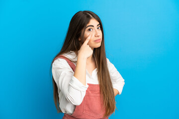 Young caucasian woman isolated on blue background showing something