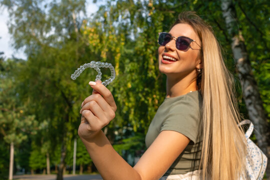 Cheerful woman in sunglasses holding an invisible teeth aligner while smiling