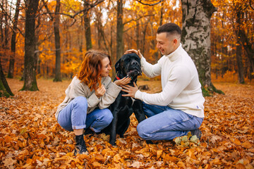 Young couple with a dog on a walk in the autumn forest