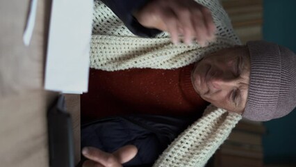 Freezing old man holding bills for electricity, gas and heating, calculating costs on calculator. Global energy crisis concept. Cold home