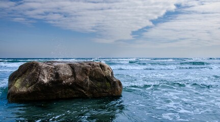 Rock formation in the middle of an ocean on a cloudy day