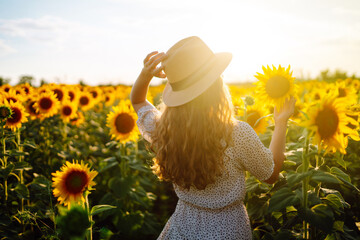 Beautiful woman strolling through field with sunflowers. Fashion, lifestyle, travel and vacations concept.