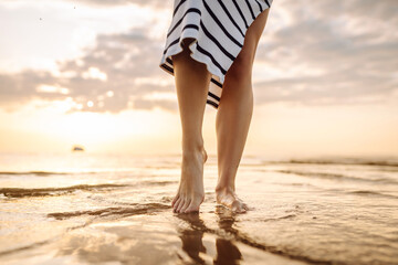 Close- up leg of young woman walking along wave of sea water and sand on the summer beach. Sexy lean and tanned legs. Summer holidays.