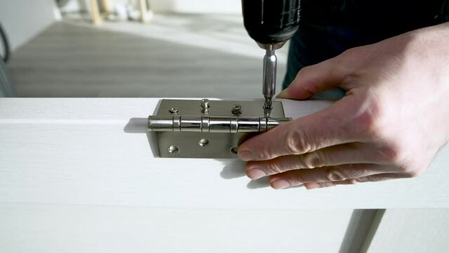 Worker is screwing a door hinge with screws. Repair and decoration of apartments. Carpentry work. Door installation.