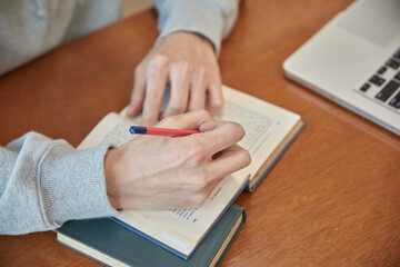 Close-up photo of a hand working with a pencil or pen on a book or notebook at a brown desk, doing work, homework, etc.