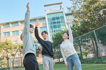 Three young male and female college models walk with a ball and raise their hands in celebration...