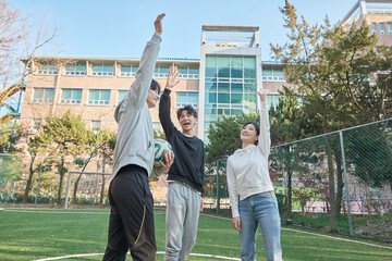 Three young male and female college models walk with a ball and raise their hands in celebration...